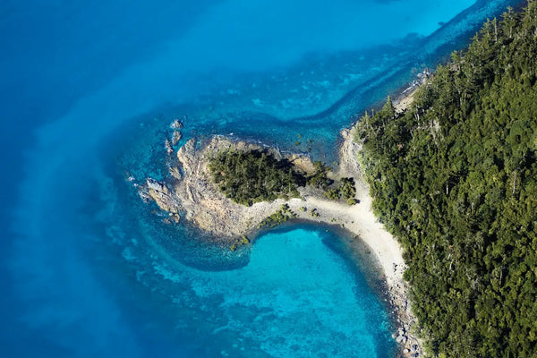 Swivel aerial photo, The Whitsundays, Queensland. Tropical blue sea meets white sand and green headland.