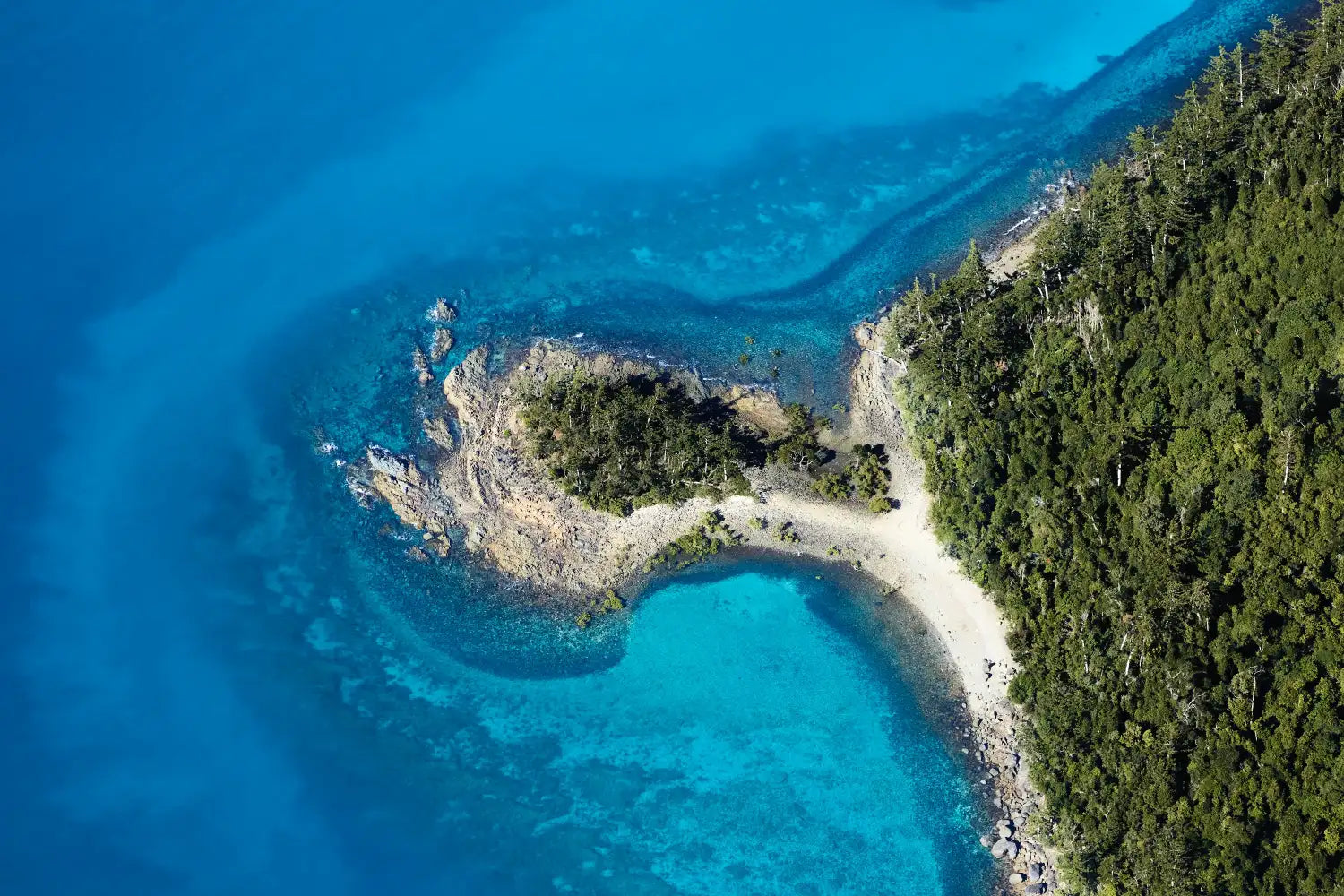 Swivel aerial photo, The Whitsundays, Queensland. Tropical blue sea meets white sand and green headland.